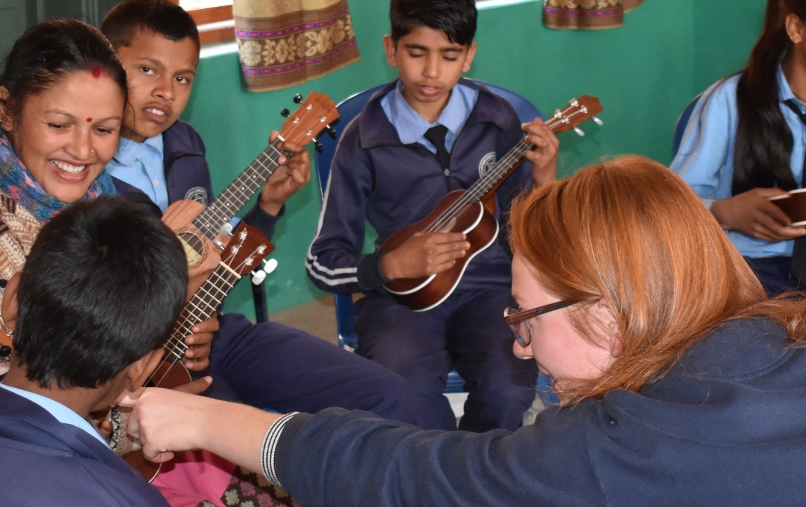 Groepje leerlingen en juf met ukelele. Sike wijst naar de ukelele die een van de leerlingen in de hand heeft.